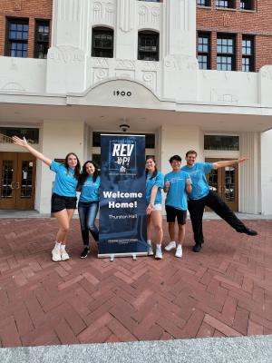 A group of CLRE student staff (CEAs and CEAds) have fun working together during the GW Move-In process, standing in front of Thurston Hall and wearing matching blue shirts.